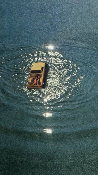 An aerial view shows a yellow pickup truck driving through water, creating ripples and reflections on the surface.
