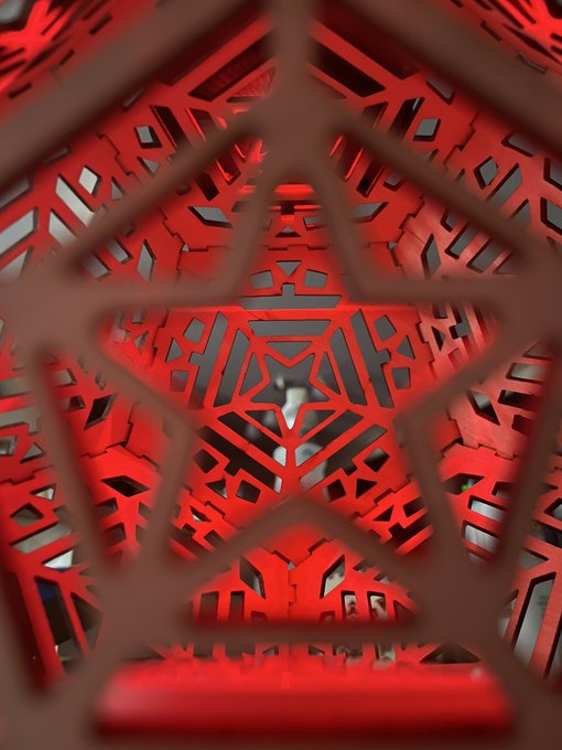 A close-up macro shot of an intricate red laser-cut geometric pattern with triangular shapes forming a kaleidoscopic tunnel-like design.