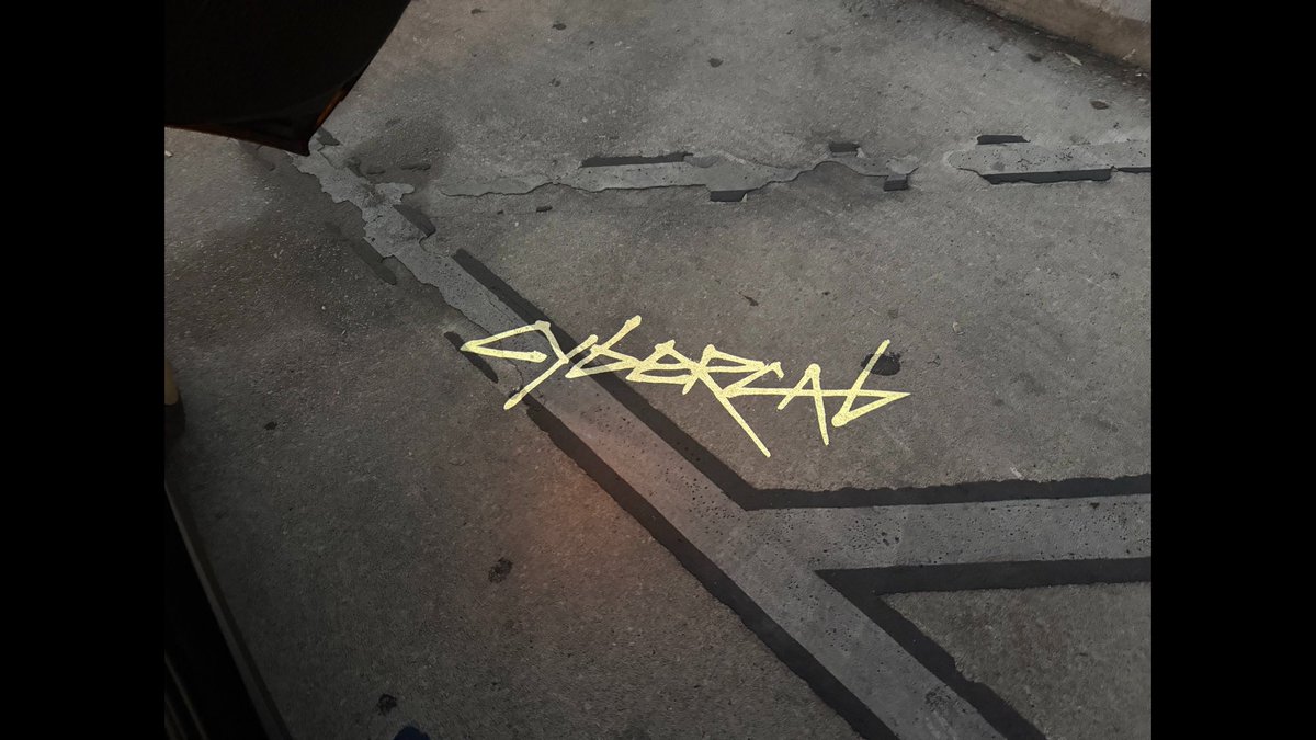A concrete surface with a yellow graffiti tag that appears to read 'CYBERPUNK' in a stylized, angular font.