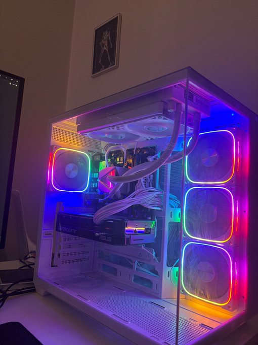 A white PC case with transparent panels showcases internal components illuminated by colorful RGB lighting in blue, pink, and yellow hues.