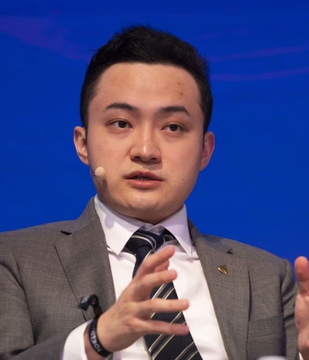 Justin Sun, founder of HTX (formerly Huobi), speaks at a conference while wearing a gray suit and striped tie, gesturing with his hands as he addresses the audience. His image accompanies a statement in which he clarifies that Binance's restrictions on HTX-related transactions apply only to users in the UK and EU.