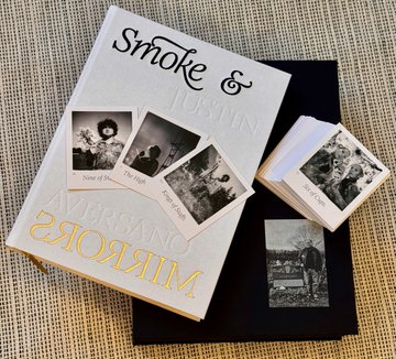A photo of the "Smoke & Mirrors" book by @justinaversano, with black and white portraits visible on the cover and a stack of additional portrait cards beside it. The accompanying praise for the beautiful book aligns with the elegant, artistic presentation of the book in the image.