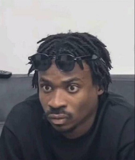 A close-up photo of a man with dreadlocks and sunglasses perched on his head, staring directly at the camera with a wide-eyed expression.