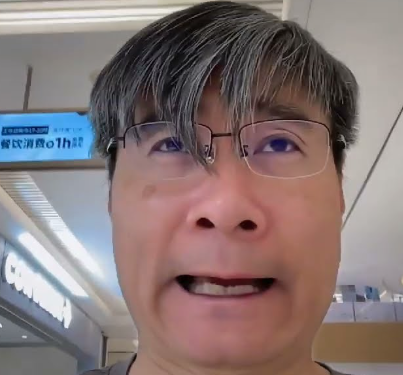 A man with glasses takes a selfie video inside what appears to be a Japanese train, with a sign reading '花火の1h' (1 hour of fireworks) visible in the background.