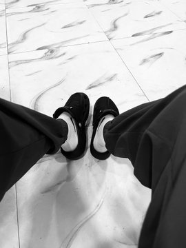 A black and white photo looking down at a person's feet wearing black and white sneakers standing on a marble floor.