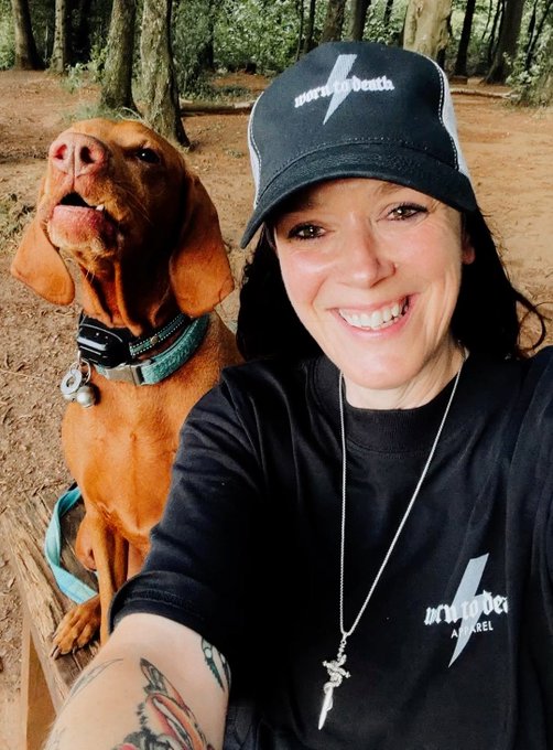 A woman wearing a black "Unicorn Auth" cap and matching t-shirt smiles for a selfie alongside a happy Vizsla dog in a wooded setting, capturing the cheerful Friday vibe of the accompanying post celebrating the NFT Community.
