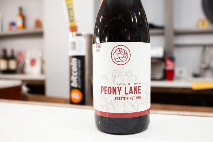A bottle of Peony Lane Estate Pinot Noir 2023 wine sitting on a white countertop in what appears to be a bar setting.