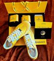 A pair of yellow and white sneakers with a "X" design, displayed in front of its black and yellow box.