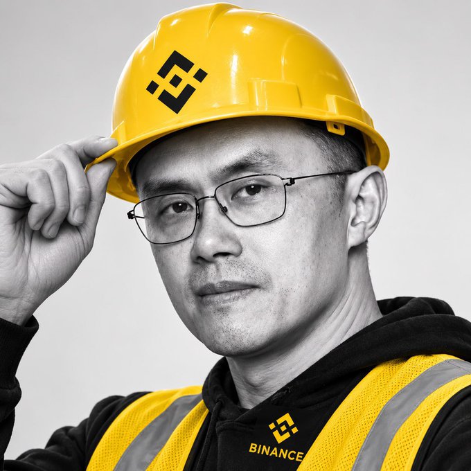 The image shows a man in black-and-white wearing a yellow hard hat with the Binance logo and a yellow safety vest with the text "BINANCE," likely representing a crypto "builder." The hard hat and vest visually reinforce the post's theme of hands-on work and travel, symbolizing on-the-ground effort rather than delegated social media management.
