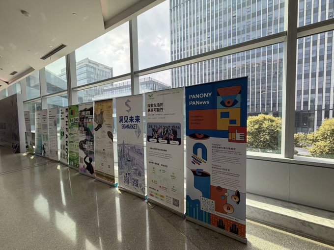 A row of vertical exhibition banners, including ones for 'SUMACKET' and 'PANONY PANews,' lines a bright corridor with large windows overlooking trees and buildings.