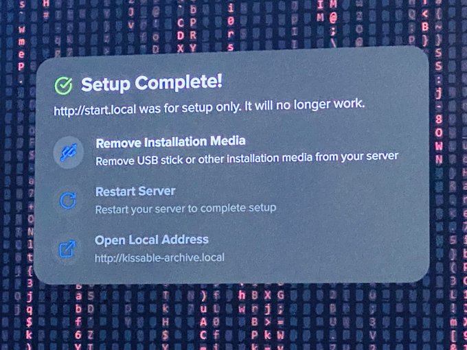 A computer screen displays a 'Setup Complete!' message with options to 'Remove Installation Media,' 'Restart Server,' and 'Open Local Address' at http://kissable-archive.local.