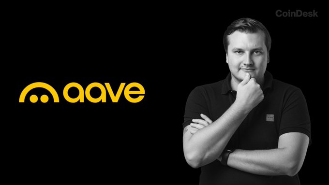 A man in a black polo shirt poses thoughtfully with his hand on his chin next to the yellow "aave" logo, with the "CoinDesk" watermark in the corner—visually representing the Aave protocol mentioned in the news of its proposal to retire underused assets and smaller protocol versions.