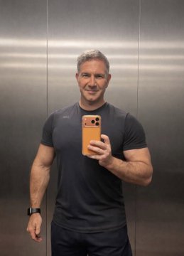Mirror selfie of a muscular man with short hair wearing a navy blue t-shirt and holding an orange iPhone.