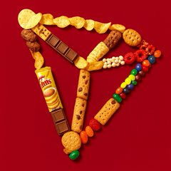 An assortment of snacks and candies—including chips, chocolate, popcorn, a bottle of Nissin soup, M&Ms, and granola bars—is creatively arranged to form a pizza slice shape on a red background.