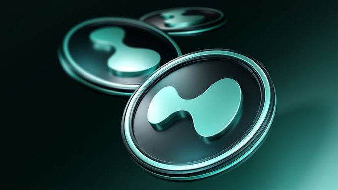 A 3D render shows three circular coins or tokens with a cyan-tinted hourglass-like logo on a dark teal background, resembling cryptocurrency iconography.