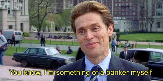 A man in a dark suit and blue tie smiles smugly in an outdoor urban setting with cars and pedestrians in the background; a yellow subtitle reads, 'You know, I'm something of a banker myself'.