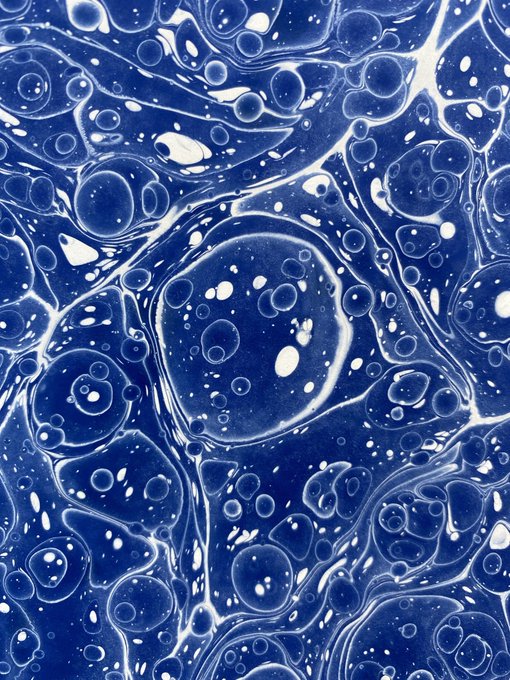 An abstract fluid art piece featuring deep blue tones with white bubbles and swirling organic patterns resembling cells or marbled textures.