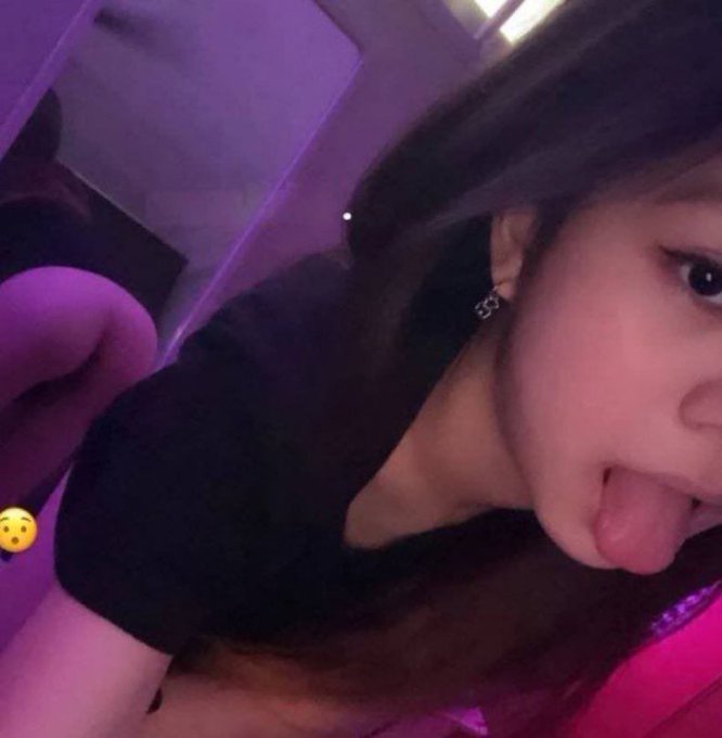 A close-up selfie shows a young woman with long dark hair sticking her tongue out playfully toward the camera, bathed in purple lighting, wearing earrings with "SSY" visible. The image ties into the post "first post wanna trade?" by serving as an introductory visual to establish the poster's identity and playful personality.