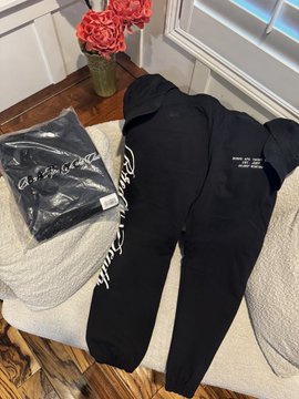 A pair of black sweatpants laid out on a cushion next to a packaged black t-shirt, both featuring white 'newjeans' text branding.