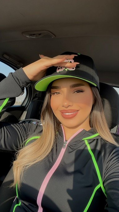 A woman in a black and pink tracksuit and a black baseball cap with a green brim and a white logo smiles and adjusts her hat. The logo on the hat is not clearly legible but the overall image supports the post's message about building a new blockchain network from the ground up.