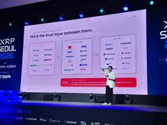 A speaker presents on a stage at XRP Seoul 2025, with a large screen displaying a chart titled 'Old is the trust layer between them.'