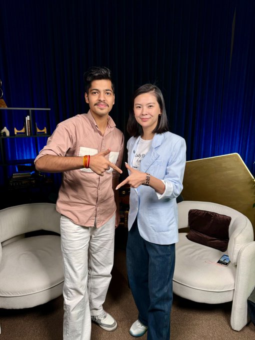 Two people pose together in a studio setting with blue curtains, where the man on the left in a pink shirt and the woman on the right in a light blue blazer both make peace signs toward the camera. The caption identifies the woman as Gracy Chen, CEO of the Bitget cryptocurrency exchange, following their meeting in Abu Dhabi.