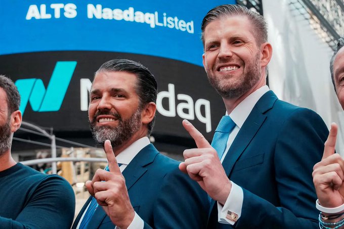 Donald Trump Jr. and Eric Trump smile and pose with crossed fingers in front of a Nasdaq billboard displaying "ALTS NasdaqListed," promoting a moment that ties into their family's crypto venture, World Liberty Financial, which is partnering with Hong Kong-based AI platform WorldClaw—an ironic juxtaposition given the post's note about Trump's tough China stance clashing with the family's crypto dealings tied to a Chinese-linked firm.