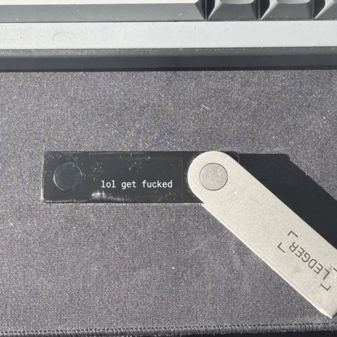 A black metal USB drive with the text 'lol get fucked' written on it, lying next to a folding multi-tool with 'LEDGER' printed on the handle.