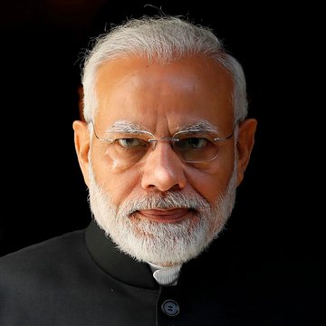 Portrait photograph of Indian Prime Minister Narendra Modi against a dark background, wearing glasses and a black bandhgala suit.