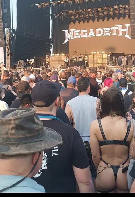 A crowd at a concert faces a stage where the band Megadeth is performing, with their name displayed prominently on the backdrop.