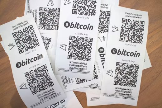 A scattered pile of pre-printed Bitcoin paper wallet QR codes, each labeled with "bitcoin," "public key," and "private key," along with serial numbers, rests on a wooden surface—representing the early 2013 method of receiving Bitcoin from eBay sellers before digital wallets became widespread.