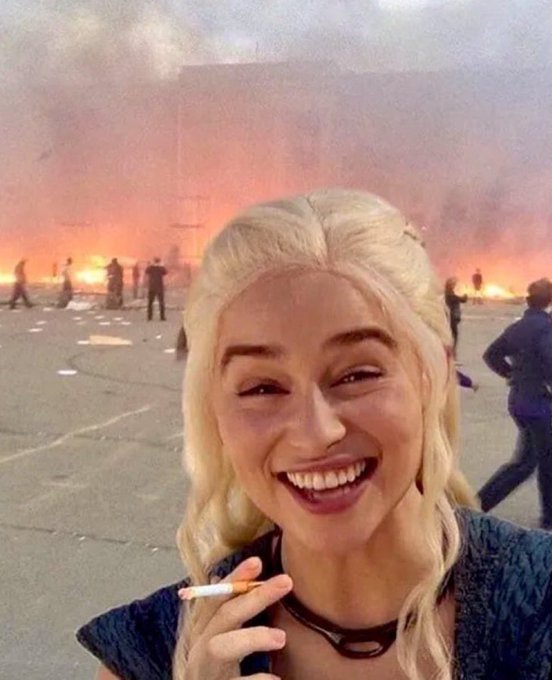 A smiling blonde woman holds a cigarette in the foreground while a chaotic scene of burning buildings and fleeing people unfolds behind her. The post humorously contrasts the devastation ("Tamra currently: burning") with her calm preparation for "Bitcoin Uptober," suggesting she remains unfazed by worldly chaos while focused on crypto gains.