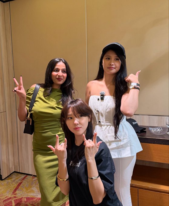 Three women pose together making hand gestures at what appears to be a BasedOneX event, with one in an olive green dress, another in a white strapless top and cap, and a third in a black "Fword" shirt making bunny ears behind the group. The post suggests they had an enjoyable meetup with great vibes at the crypto/blockchain gathering.