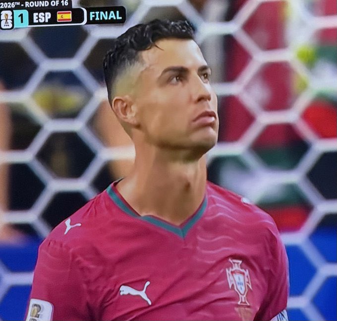 Cristiano Ronaldo in a Portugal red Puma jersey looking upward with a dejected expression, with a scoreboard showing Spain leading 1-0 in the 2026 World Cup Round of 16.