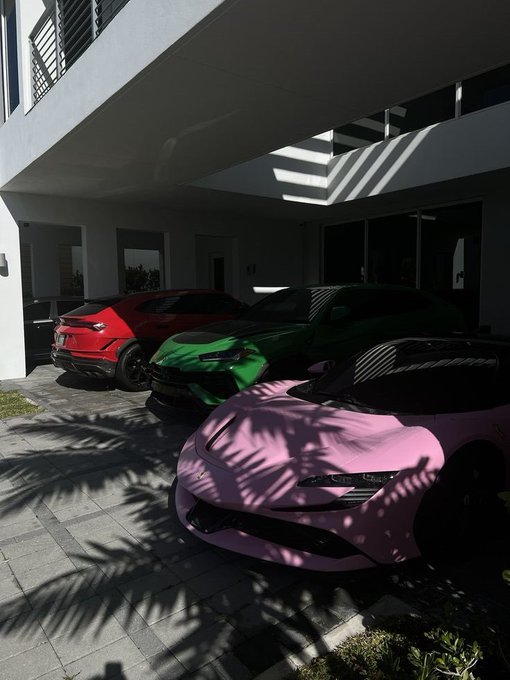 A photograph of three luxury sports cars parked in a shaded driveway: a pink car in the foreground, a green car in the middle, and a red car in the back.