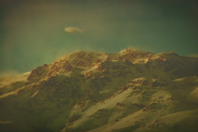 Surreal landscape with a small fish floating in the sky above snow-capped mountains under a greenish sky.