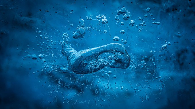 A moody, blue-tinted macro shot captures water splashing and forming bubbles, resembling an underwater explosion or fluid art.