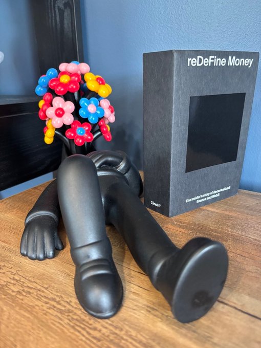 A black articulated figure lying on a wooden surface next to a colorful ball-and-stick molecular model and a box labeled 'reDeFine Money' by Unq.