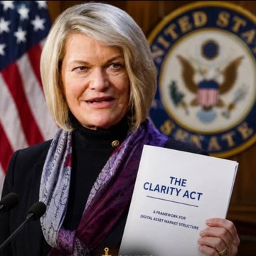 Senator Cynthia Lummis stands at a podium holding "THE CLARITY ACT — A FRAMEWORK FOR DIGITAL ASSET MARKET STRUCTURE," emphasizing her recent statement that "It is now or never" for the legislation ahead of today's pivotal Senate vote, which crypto advocates are tying to Pi Network's potential growth.