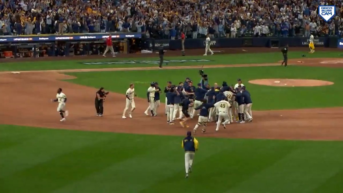 A baseball team rushing together to celebrate on the field while fans cheer in the stands, with a 'Geico Ballpark Cam' watermark in the upper right.