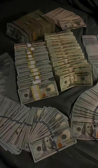 Stacks of U.S. currency, including numerous bundles of $50 and $100 bills, are arranged on a dark surface.