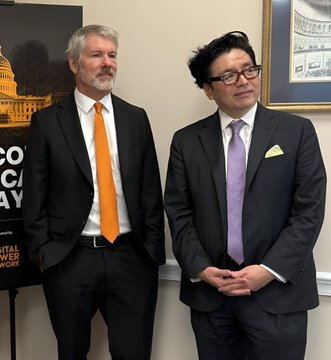 Two men in business suits standing together; the older man on the left wears an orange tie, while the younger Asian man on the right wears a purple tie and glasses.