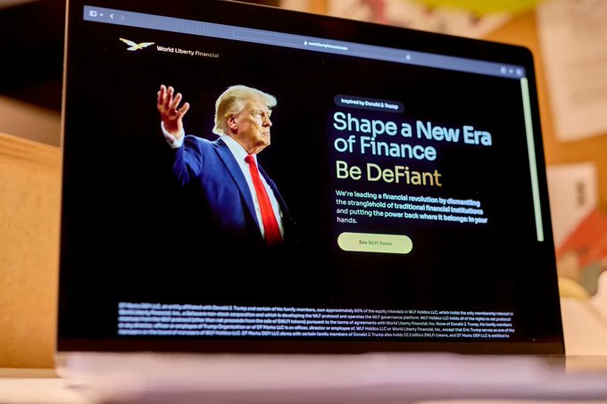 A laptop screen displays a World Liberty Financial webpage featuring Donald Trump, with the headline 'Shape a New Era of Finance. Be DeFiant.' and text about a 'financial revolution' inspired by Donald J. Trump.