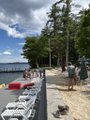 The image shows a beach scene with several people enjoying their time near the water's edge. There are at least ten individuals present, some standing or walking along the shoreline while others are sitting on chairs placed nearby. The chairs are arranged in rows, providing ample seating options for those who wish to relax and take in the view of the ocean. The beach is also adorned with trees that add a touch of nature to the scene.