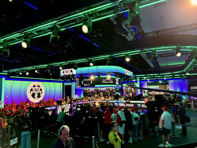 A crowded esports event stage with green and blue lighting, featuring screens showing 'POKER' and 'Final Table' signage along with 'SOLANA' branding.