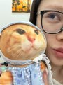A woman wearing glasses holds up a decorated cookie featuring a printed image of an orange tabby cat's face.