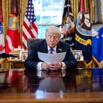 In this image, President Trump is seen in the Oval Office, appearing to read a document. This visual accompanies a report of him discussing the CLARITY Act and potentially placing his crypto in a blind trust.