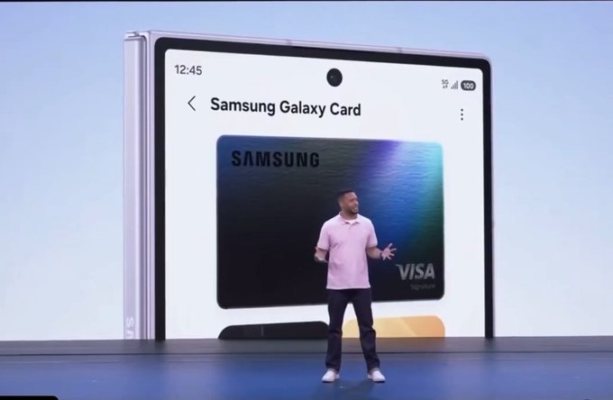 A man presents the Samsung Galaxy Card on stage, displayed on a large screen showing a Visa-branded credit card at 12:45. The image aligns with the announcement of Samsung expanding crypto payment capabilities to its billion-plus users through its built-in wallet.