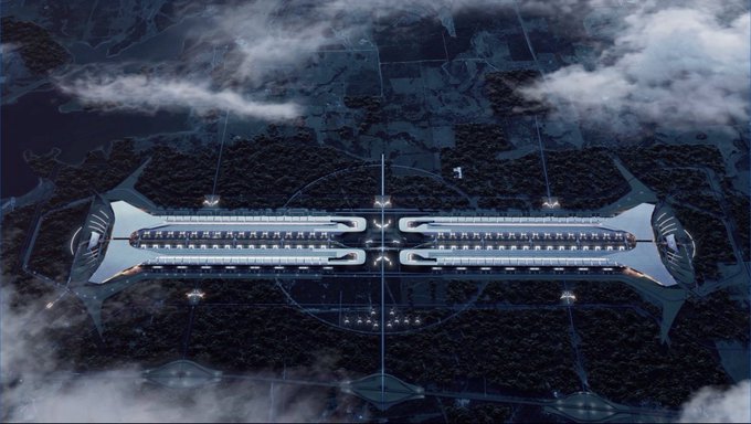 An aerial view of a massive futuristic spaceport or spacecraft facility featuring a long central structure with many docking bays, surrounded by forested terrain and clouds.