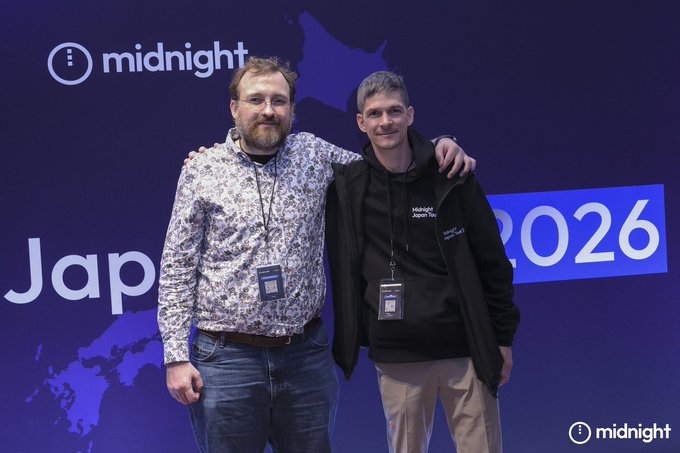 Two men pose together in front of a blue backdrop featuring the 'midnight' logo, a map of Japan, and the year '2026'.